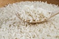 White long-grained rice on a wooden spoon on a pile of rice.