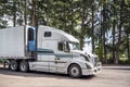 Powerful big rig semi truck with refrigerated semi trailer take a brake resting on rest area parking lot in evergreen forest Royalty Free Stock Photo