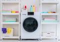 Laundry machine with washing powder. liquid and equipments on side shelf with clean colorful clothes