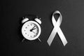 White lung cancer awareness ribbon and alarm clock on black background. November lung cancer awareness month