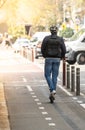 White man from behind with backpack and bicycle helmet on an electric scooter on a bike path in Barcelona along a street with