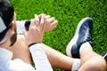 A white man in black shorts and a white shirt looks at a sports watch and adjusts it