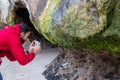 White man with a red jacket taking a very close photo with his smartphone of a rock in cathedral cove beach, Te Whanganui-A-Hei Ma Royalty Free Stock Photo