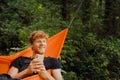 White man resting in hammock using cellphone while hiking in green forest