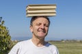 White man with white t shirt carries three large books balanced on his head on a sunny day Royalty Free Stock Photo