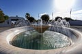 A white, marble fountain standing in a small circular square. Clear water gushes from the fountain Royalty Free Stock Photo