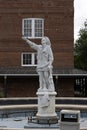 A white marble statue of Christopher Columbus at Columbus Plaza surrounded by red brick buildings and lush green trees