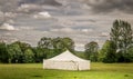 A white marquee tent in a field with rain clouds.