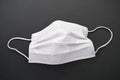 White mask with rubber ear straps on dark background. Typical 3-ply surgical mask to cover the mouth and nose. Procedure mask from