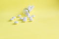 White medical pills from glass bottle on light yellow background