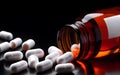 White medical pills spilling out of a drug bottle on black background Royalty Free Stock Photo