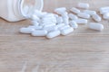 White medical pills spilling out of a drug bottle on a wooden backgrounds Royalty Free Stock Photo
