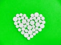 White medicine pills in the shape of a heart on a green background top view with copy space. Royalty Free Stock Photo