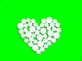 White medicine pills in the shape of a heart on a green background top view with copy space. Royalty Free Stock Photo