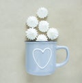 The white merengues in a cup on beige background, flat lay, top view. A blue cup with heart