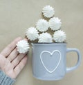 The white merengues in a cup on beige background top view. A cup with heart in women hand