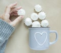 The white merengues in a cup on beige background top view. A cup with heart in women hand