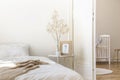 White metal bedside table with coffee mug, twig in glass vase and simple poster in frame placed by the bed