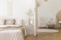 White metal bedside table with decor and coffee mug placed by the bed in bright bedroom interior with door to newborn baby room