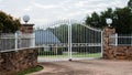 White metal wrought iron driveway property entrance gates set in brick fence, garden trees in background Royalty Free Stock Photo