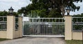 White metal wrought iron driveway property entrance gates set in concrete brick fence with coach lights, garden shrubs and trees i Royalty Free Stock Photo