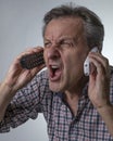 A white man yells while holding two cordless phones, with an expression of great stress Royalty Free Stock Photo