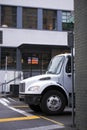 White middle size semi truck on city street surrounded by buildings