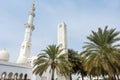 White minaret of the Grand Mosque built with marble stone and green palm trees, also called Sheikh Zayed Grand Mosque in Abu