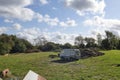 White mini van parked next to a muck heap cow waste pile in a grass area with cloudy day on Organic farm.