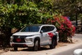 White Mitsubishi Pajero Sport parked on the street near green trees and red flowers