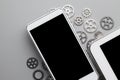 White mobile phone with black screen and small gears on gray table Royalty Free Stock Photo