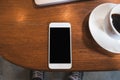 A white mobile phone with blank black desktop screen and a computer laptop with coffee cup on wooden table Royalty Free Stock Photo