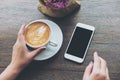 White mobile phone with blank black screen and hand holding hot latte coffee on vintage wood table in cafe Royalty Free Stock Photo