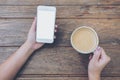 White mobile phone with blank white screen and hand holding hot coffee on vintage wood table in cafe Royalty Free Stock Photo