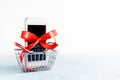 White mobile phone with red ribbon in shopping basket on white background. Gift, sale Royalty Free Stock Photo