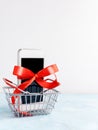 White mobile phone with red ribbon in shopping basket on white background. Gift, sale Royalty Free Stock Photo