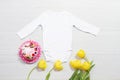 White mockup baby newborn shirt. Wooden background, yellow tulips, happy birthday pink cake. Blank template jumpsuit bodysuit Royalty Free Stock Photo
