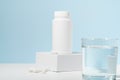 White mockup of a jar of pills on a pedestal and a glass of water on a blue background. Concept of pharmacy, medicine, health care Royalty Free Stock Photo
