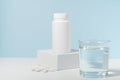 White mockup of a jar of pills on a pedestal and a glass of water on a blue background. Concept of pharmacy, vitamins, dietary Royalty Free Stock Photo