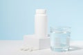 White mockup of a pill jar on a pedestal and a glass of water on a blue background. Concept of medicine, pharmacy, vitamins for Royalty Free Stock Photo
