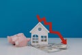 White model of house and broken piggy bank with down arrow. Falling of real estate market prices Royalty Free Stock Photo