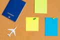 White model of passenger plane with blue passport and blue, orange, yellow paper note pin on cork board. Blank notes for add text Royalty Free Stock Photo