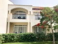 A white modern cottage, a villa, a house, a building with windows and a balcony and a green tree with red flowers, a royal delonis Royalty Free Stock Photo