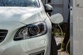 White modern plug-in car plugged and charging its battery with green electricity