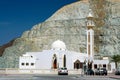 White mosque with dome and minaret in Oman in front of a rock wall