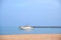 White motor boat floats in ocean water at long pier bridge under bright blue sky, view from sandy beach. Summer Royalty Free Stock Photo