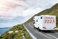 White motorhome with sign travel 2023 moving on a small mountain road and beautiful country side with ocean in foreground. Low