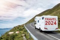 White motorhome with sign travel 2024 moving on a small mountain road and beautiful country side with ocean in foreground. Low
