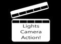 A white movie clipper board with the words lights camera action against a black backdrop Royalty Free Stock Photo