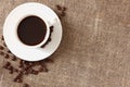 White mug with coffee, saucer and scattered coffee beans on rough burlap tablecloth, top view Royalty Free Stock Photo